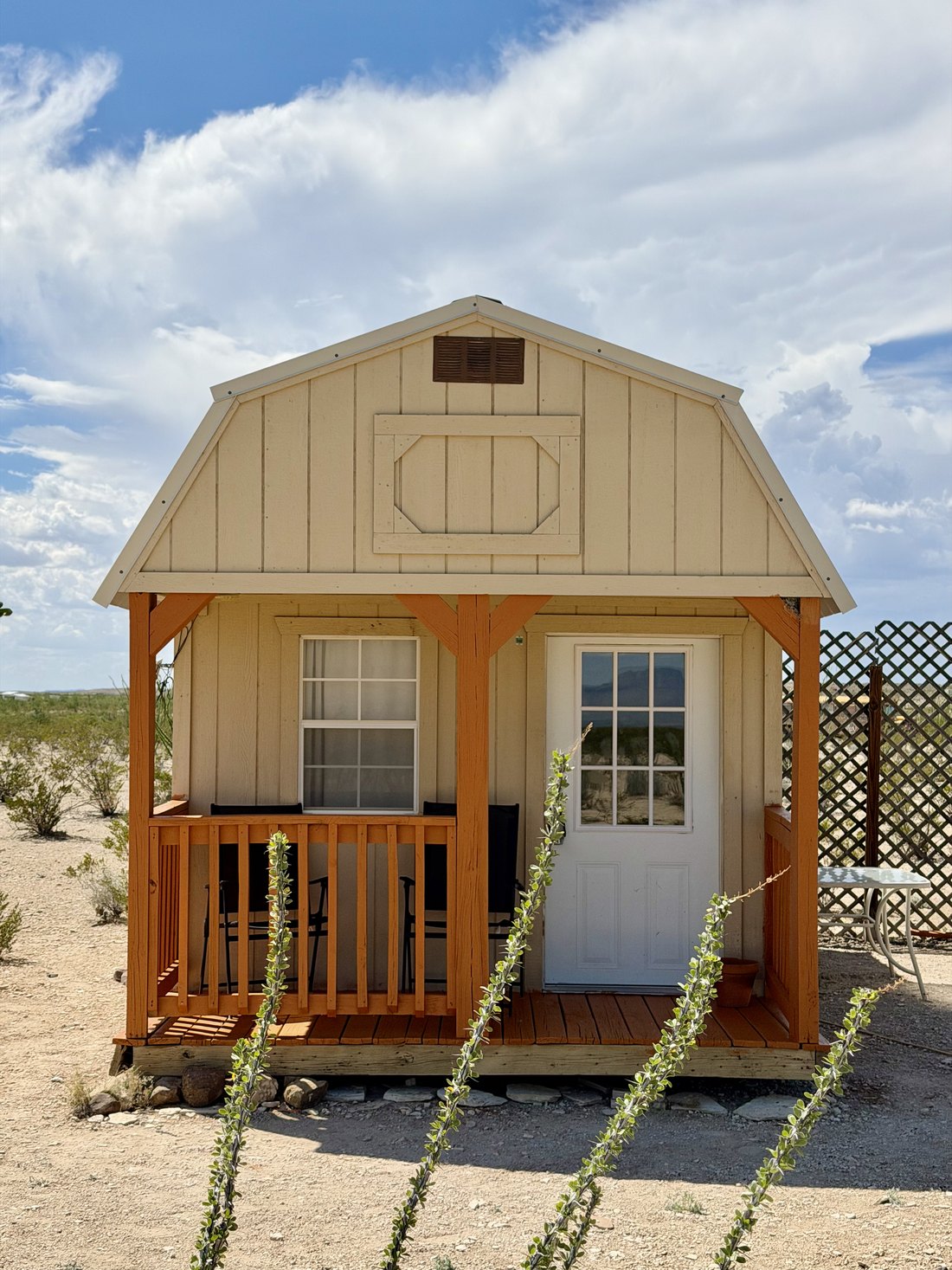 Front of the cream cabin with a covered porch, steps and a white door