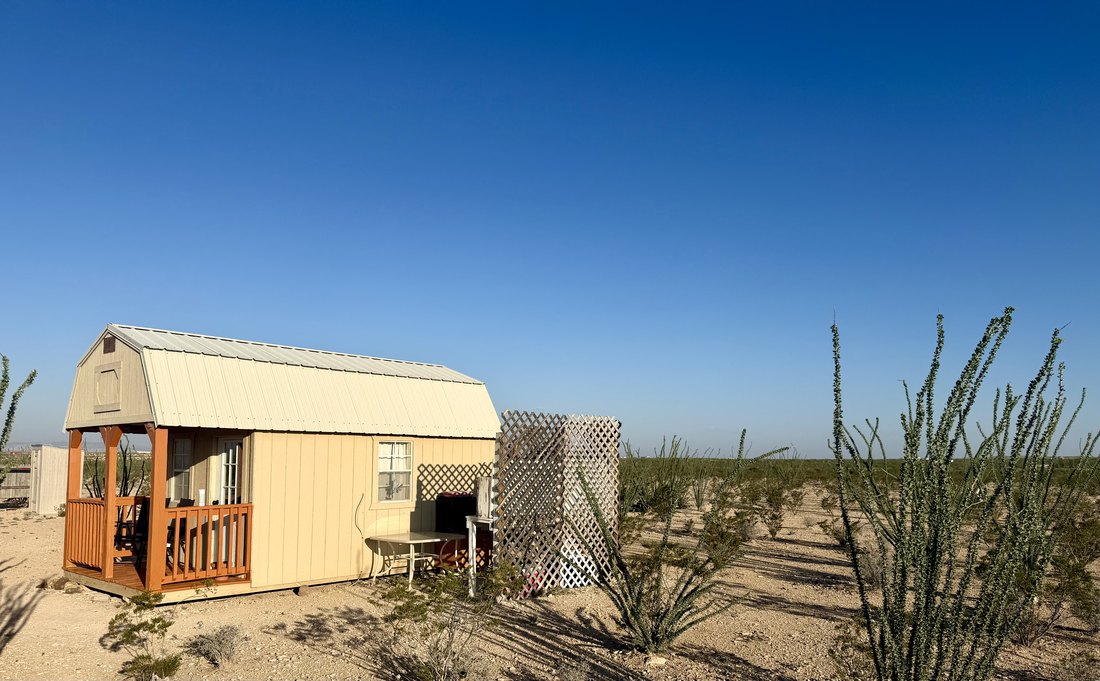 Wide view of the cabin across open desert with ocotillo in the foreground