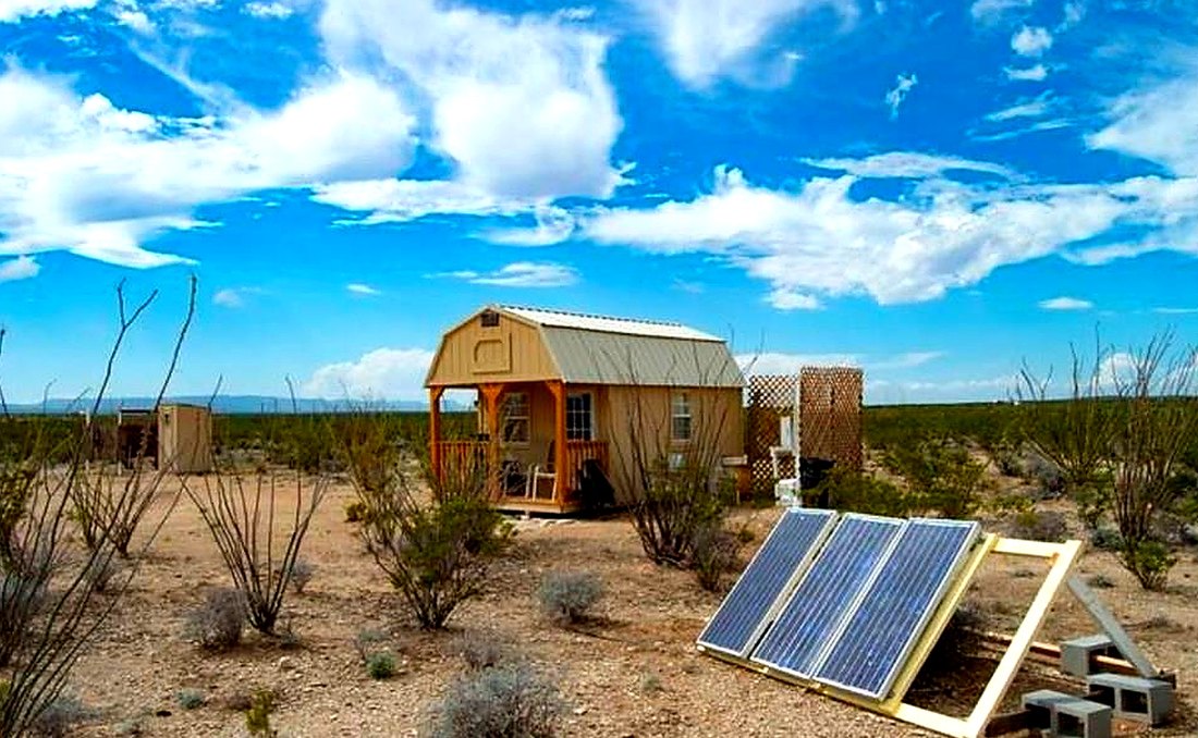 An off-grid cabin on open desert land with a ground-mounted solar array in the foreground
