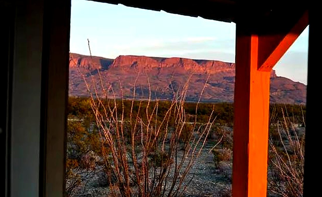 A red rock mesa at sunrise framed by the timber posts of the cabin porch